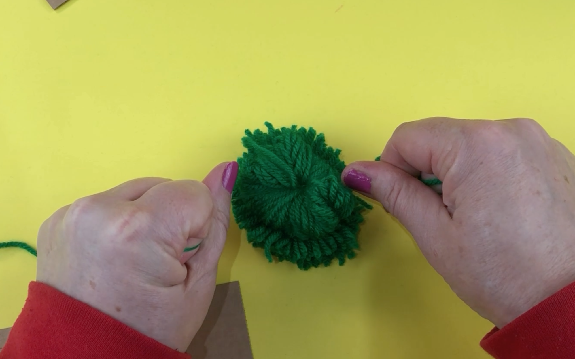 Tying the tied green wool on top of the larger piece of green wool that we tied.