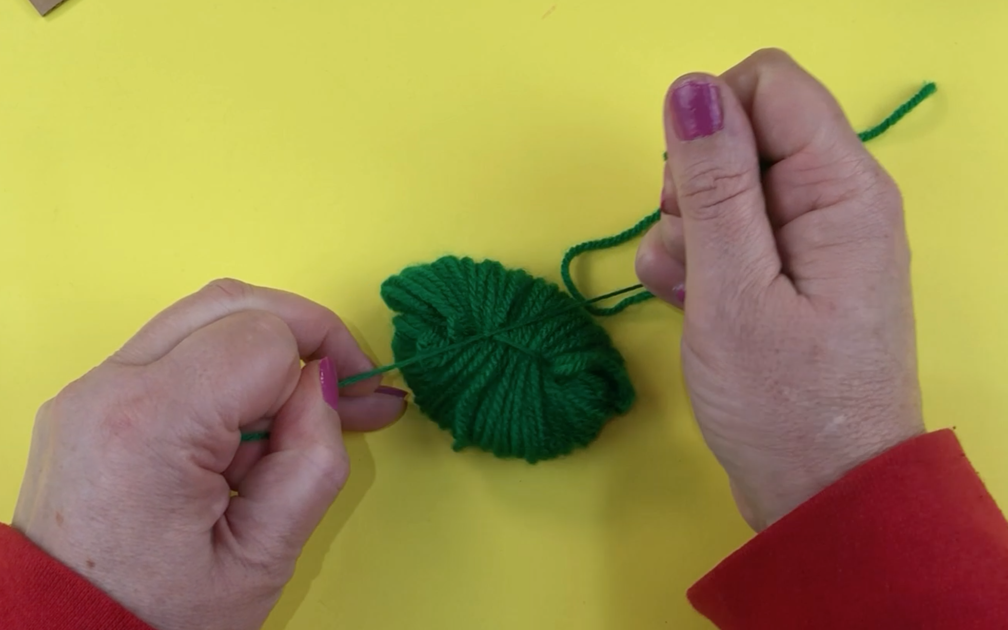 Tying the wrapped green wool with a long piece of green wool.