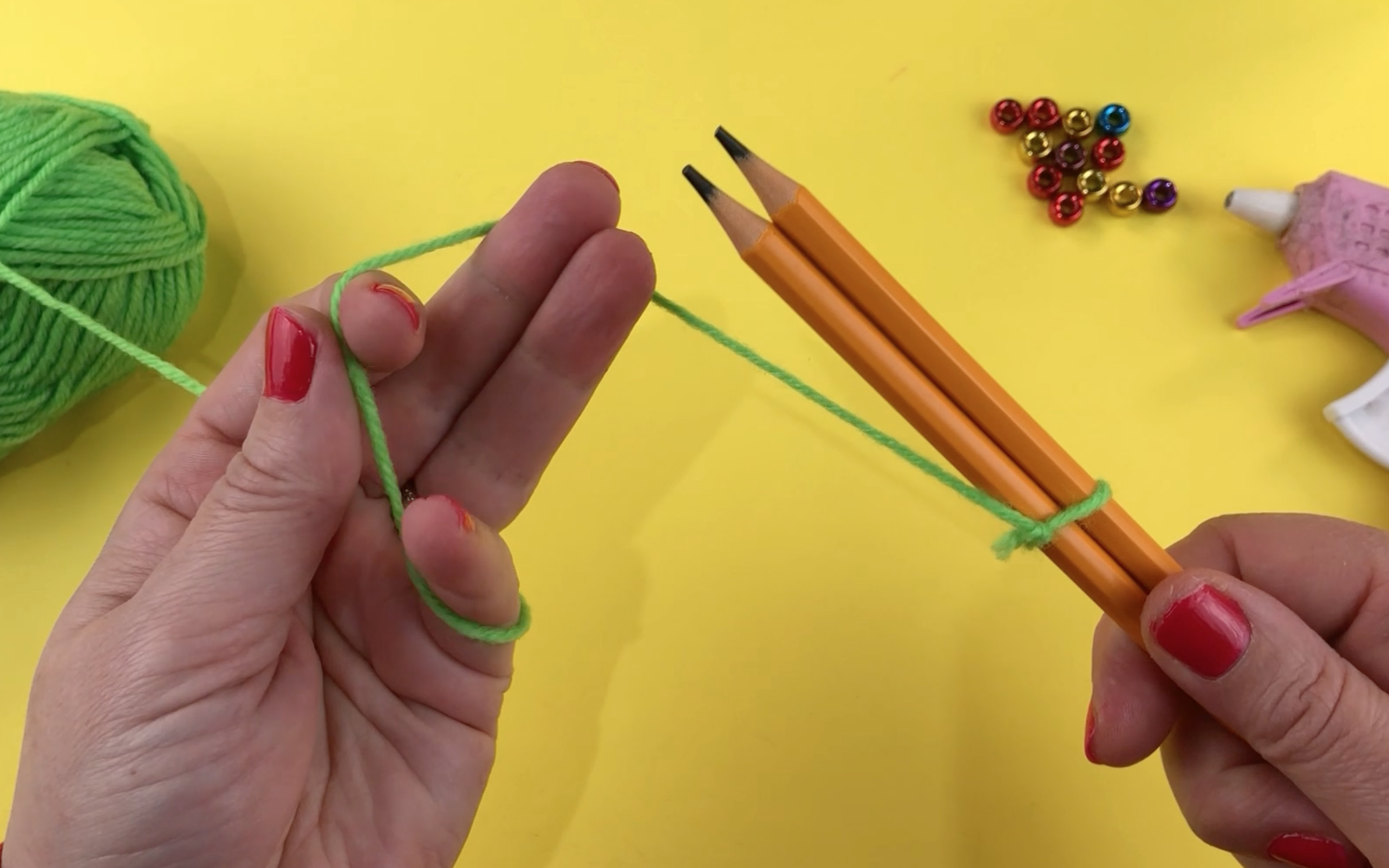 2 pencils with some green wool tied around them both. The wool is tied in a knot.