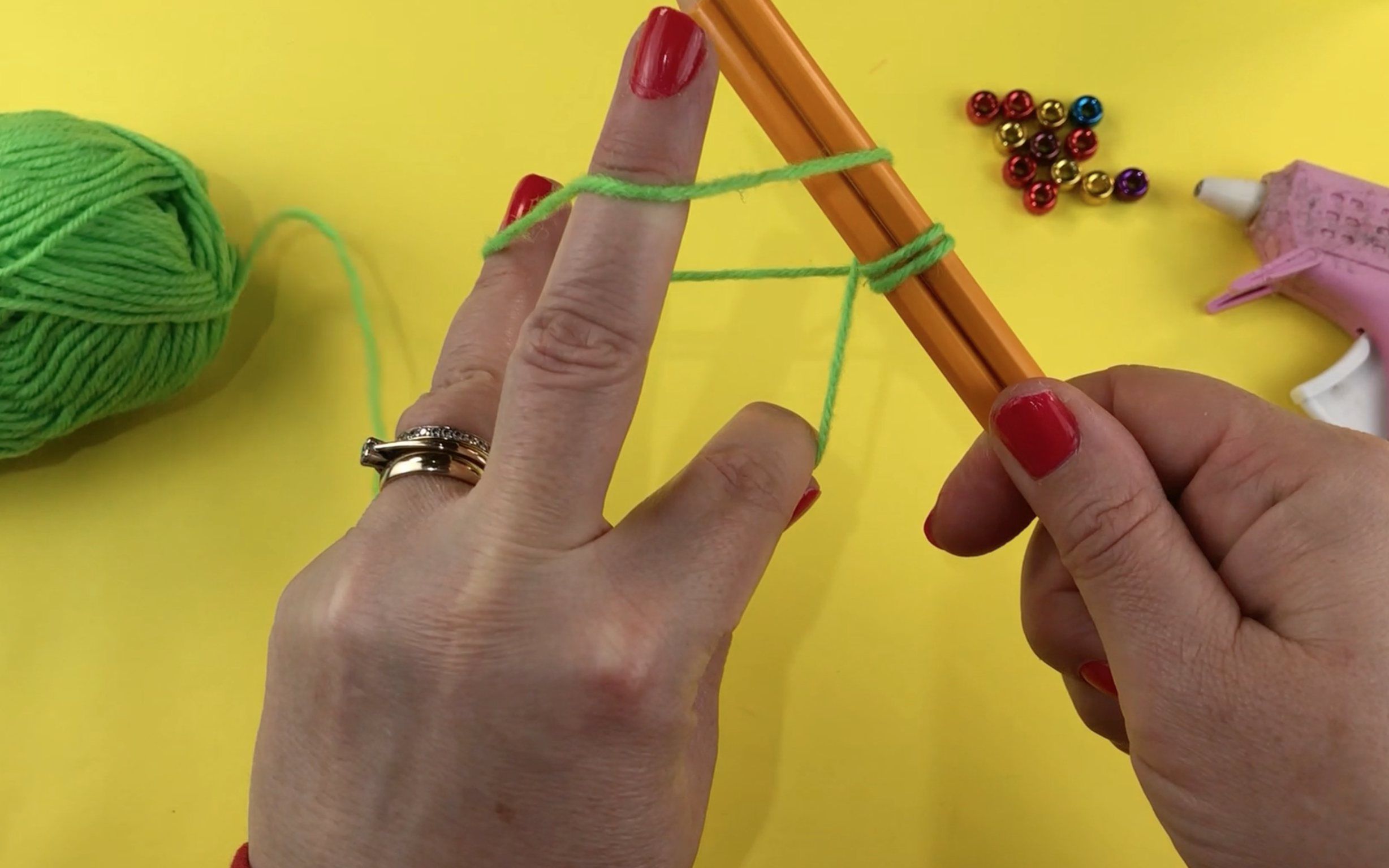 Showing the loop made using green wool and 2 pencils.