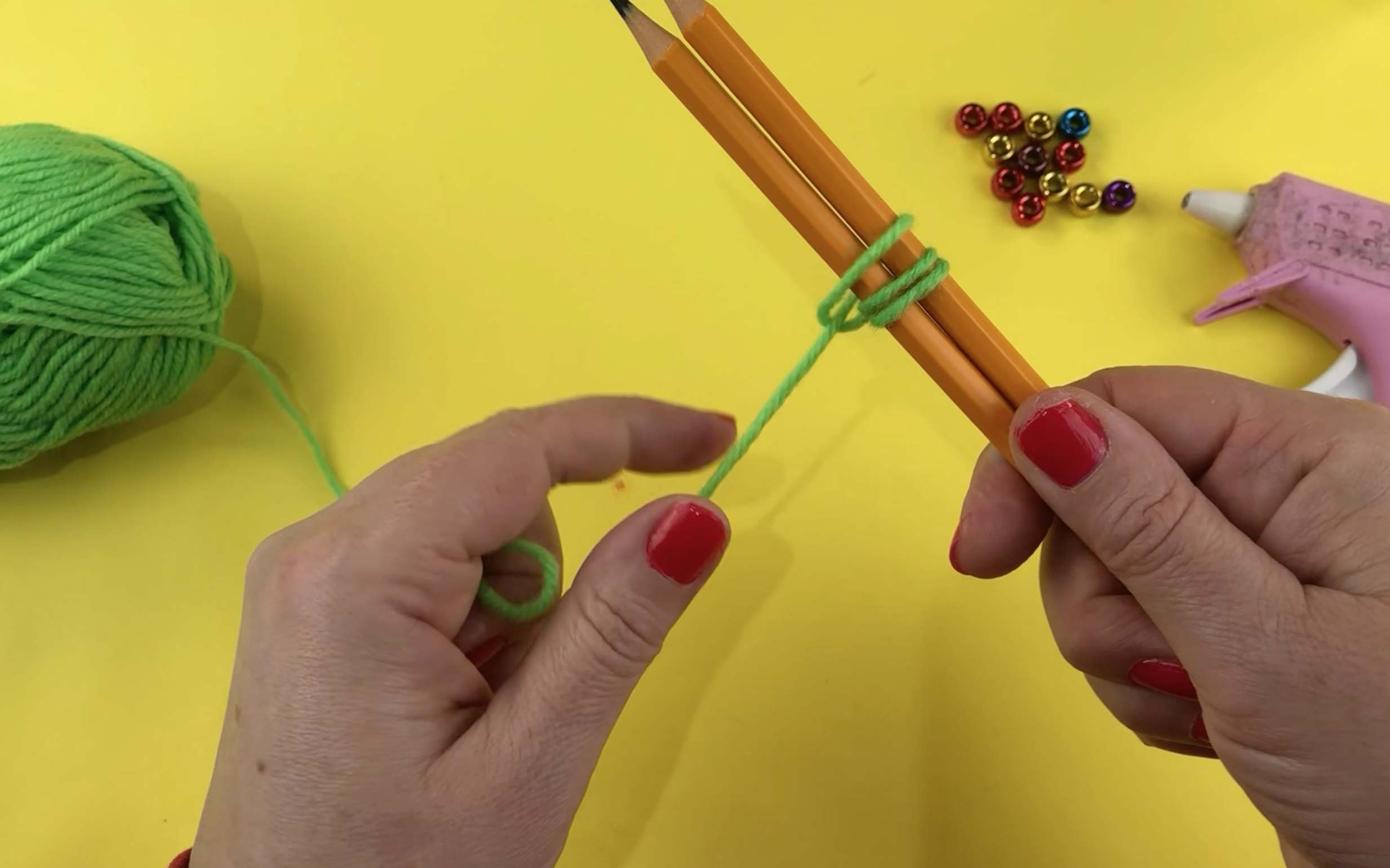 Pulling the green wool tight to make a loop around the pencils.