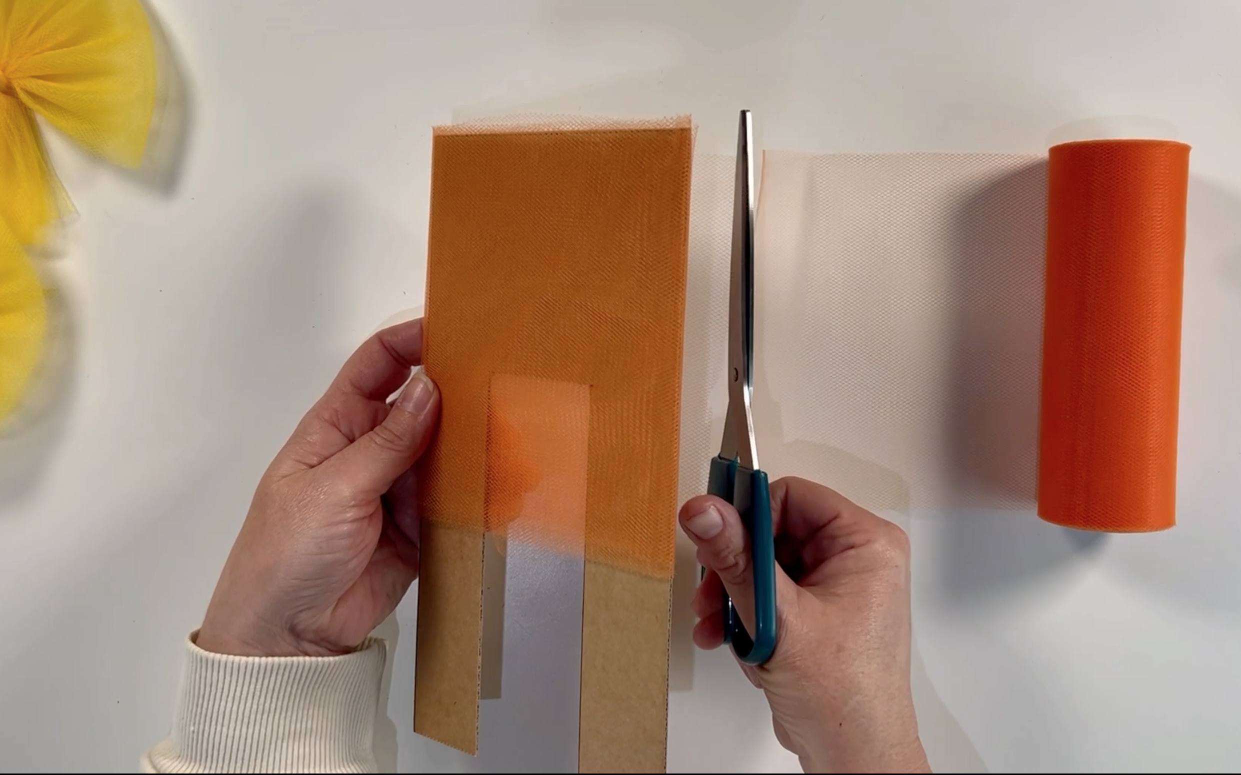 Trimming the tulle with scissors that has been wrapped around the cardboard template