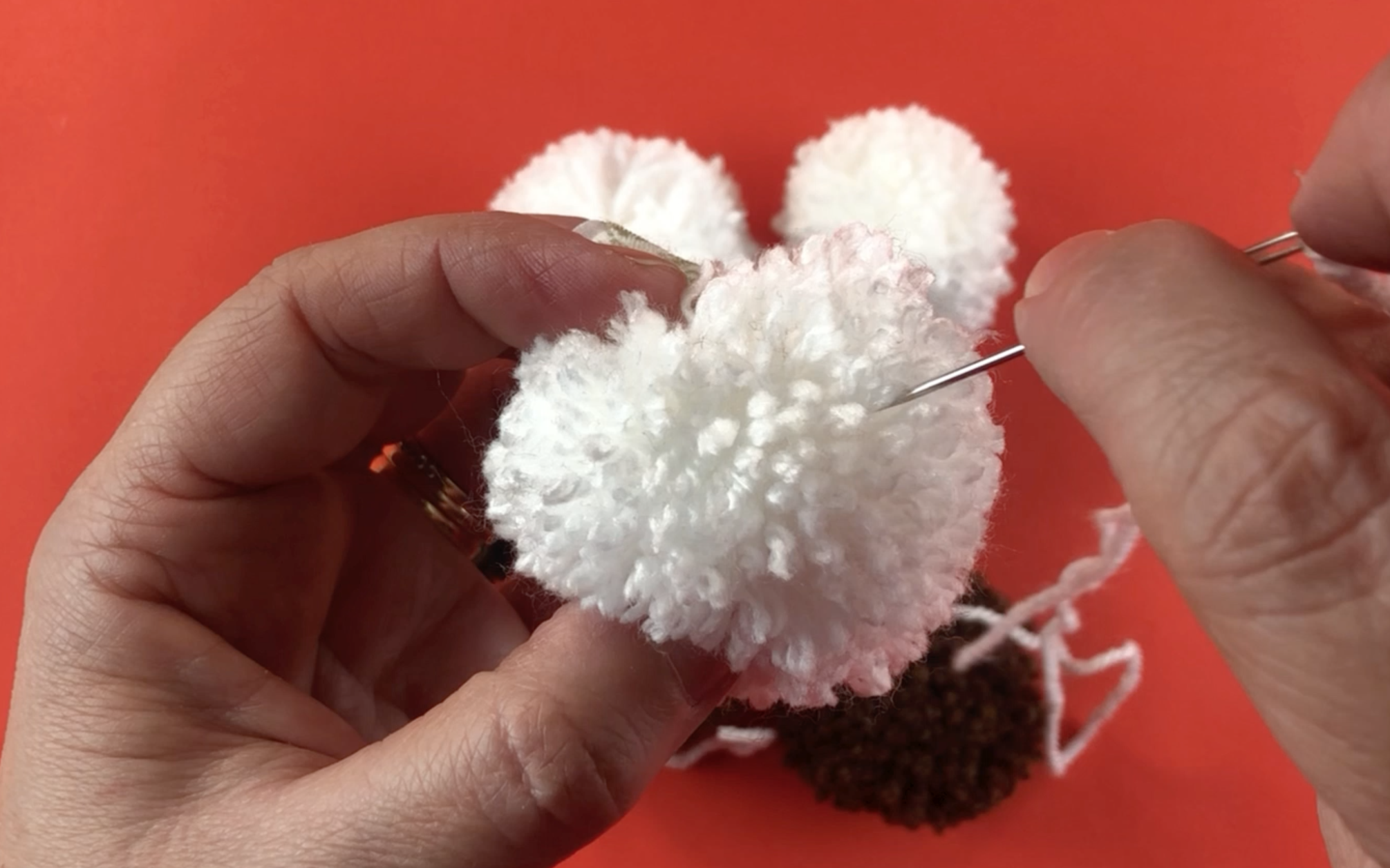 pushing the large eye needle through the centre of the white pompom