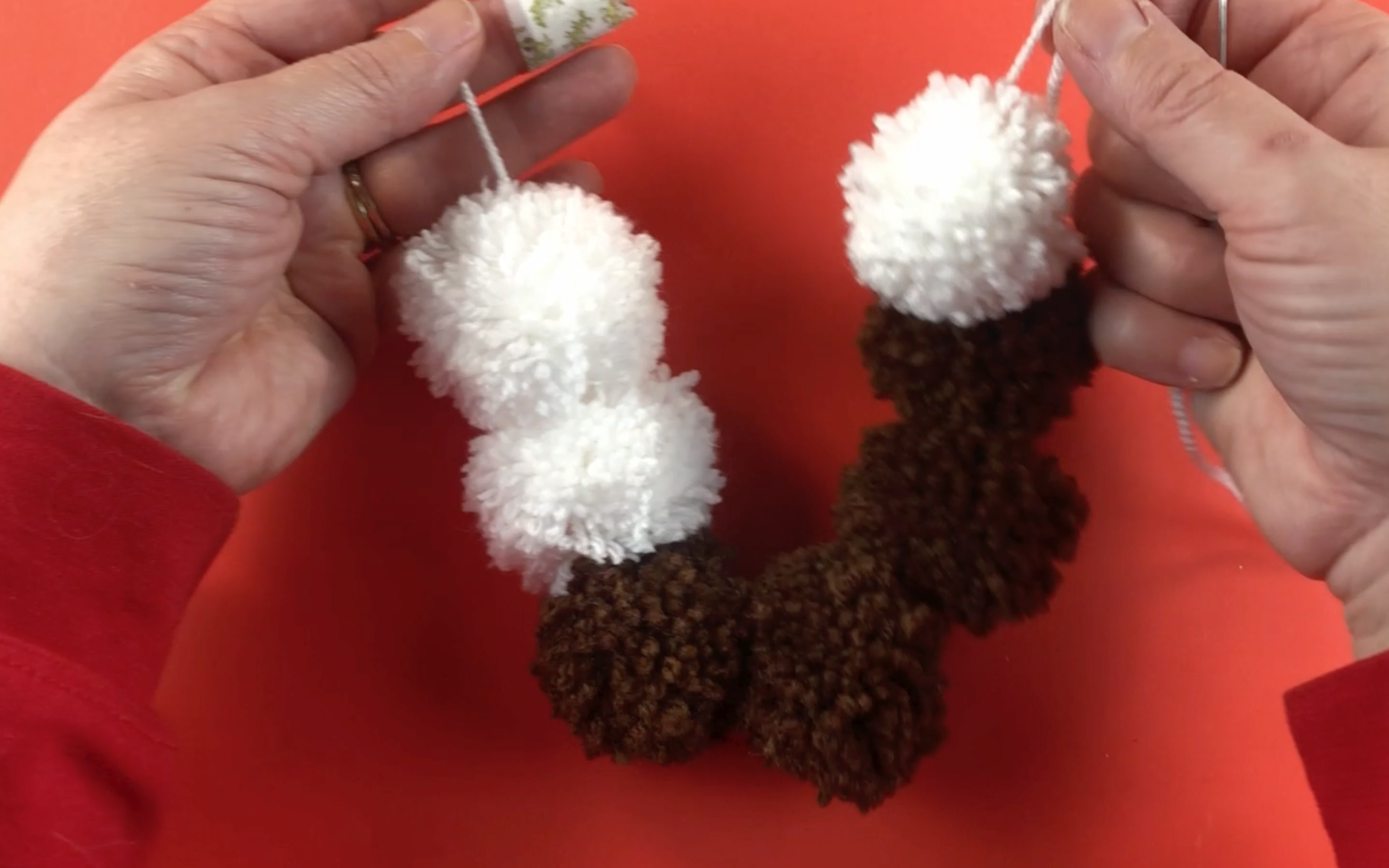 All 3 white pompoms and all 4 brown pompoms attached to the wool. The 4 brown pompoms are at the bottom