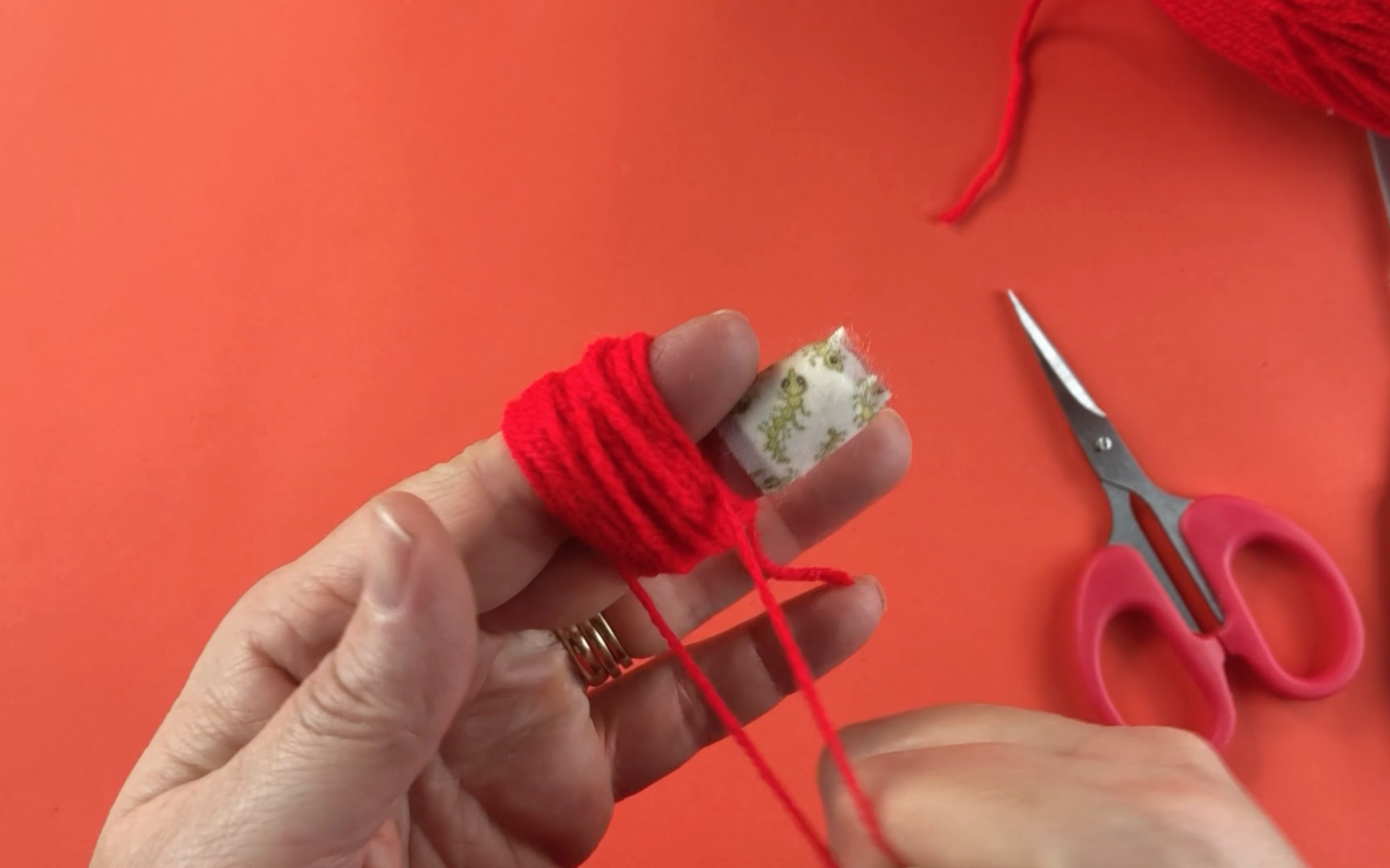 Making a small red pompom by wrapping wool around your fingers