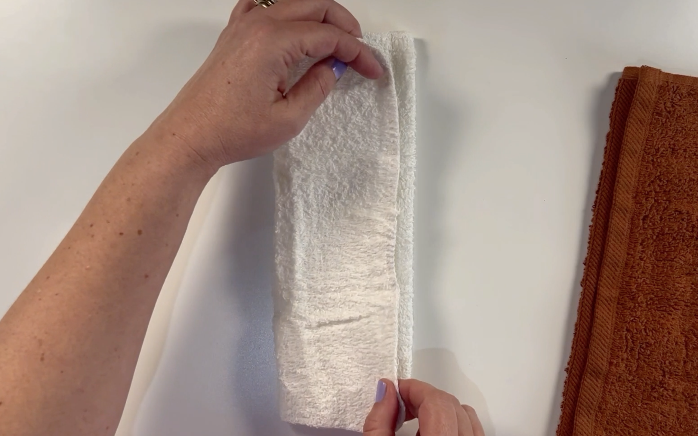 Folding the other side of the white washcloth over so that the edges meet.