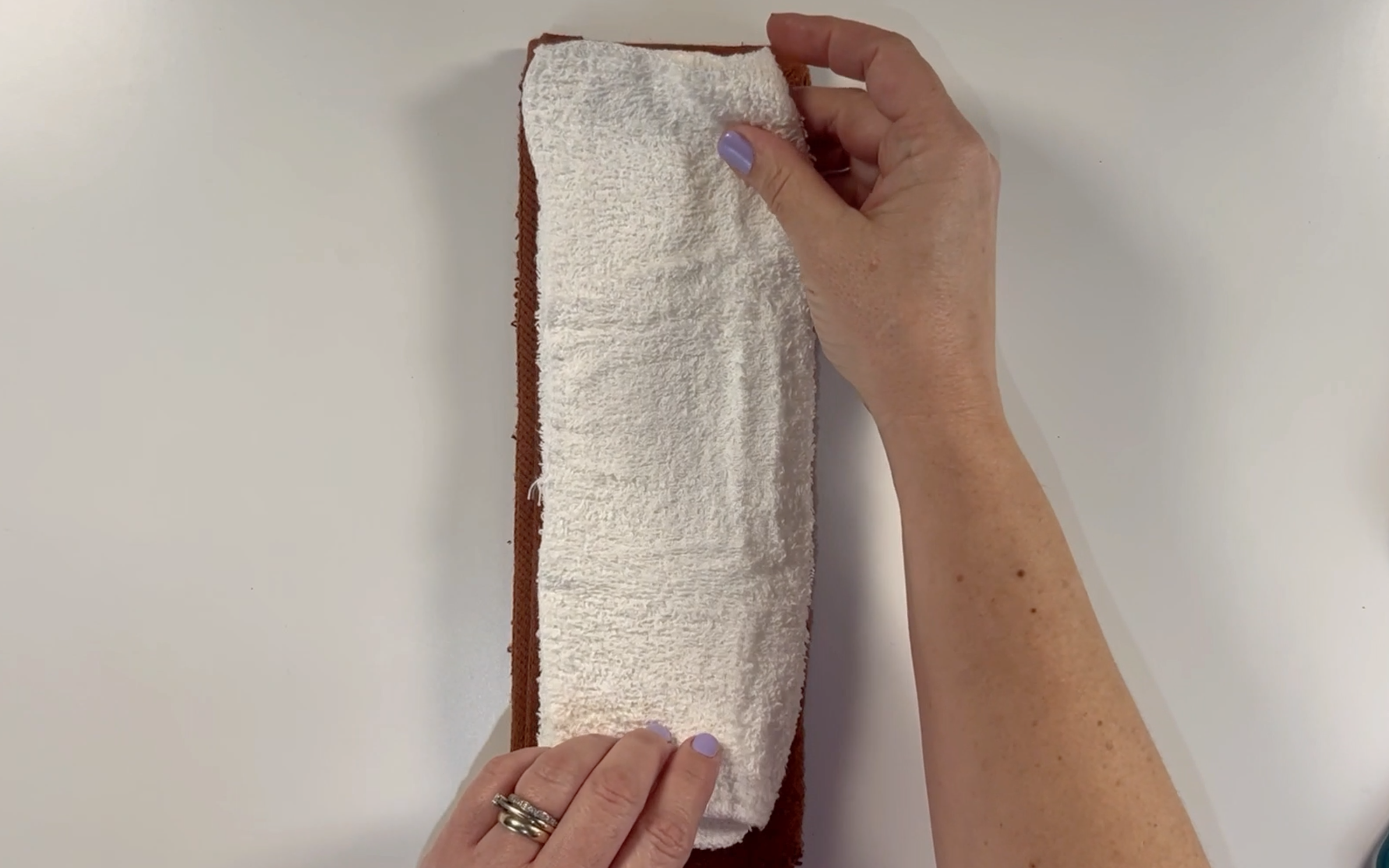 Placing the brown folded washcloth on top of the white folded washcloth