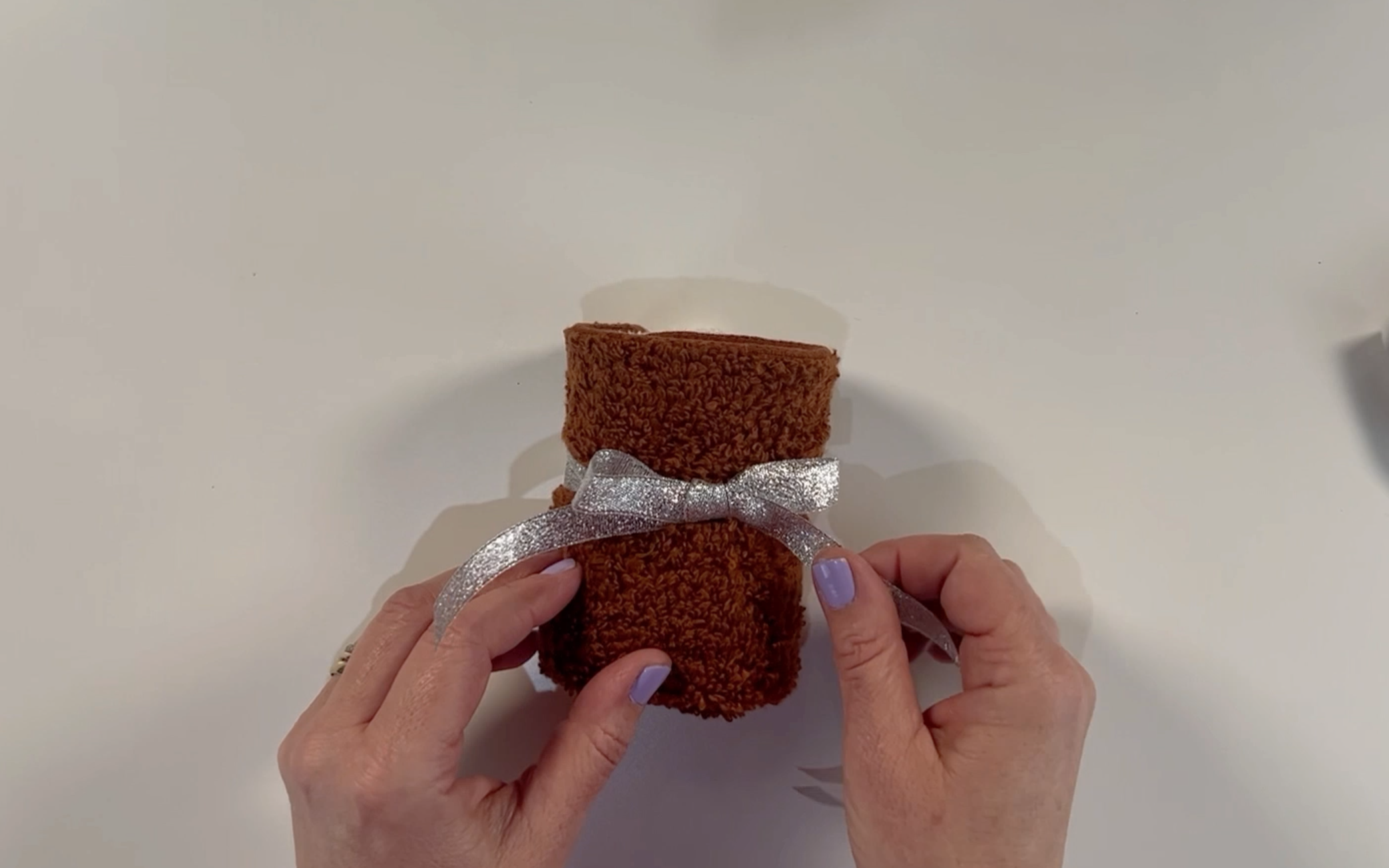 Adding a ribbon ties in a bow around the centre of the rolled wash clothes.