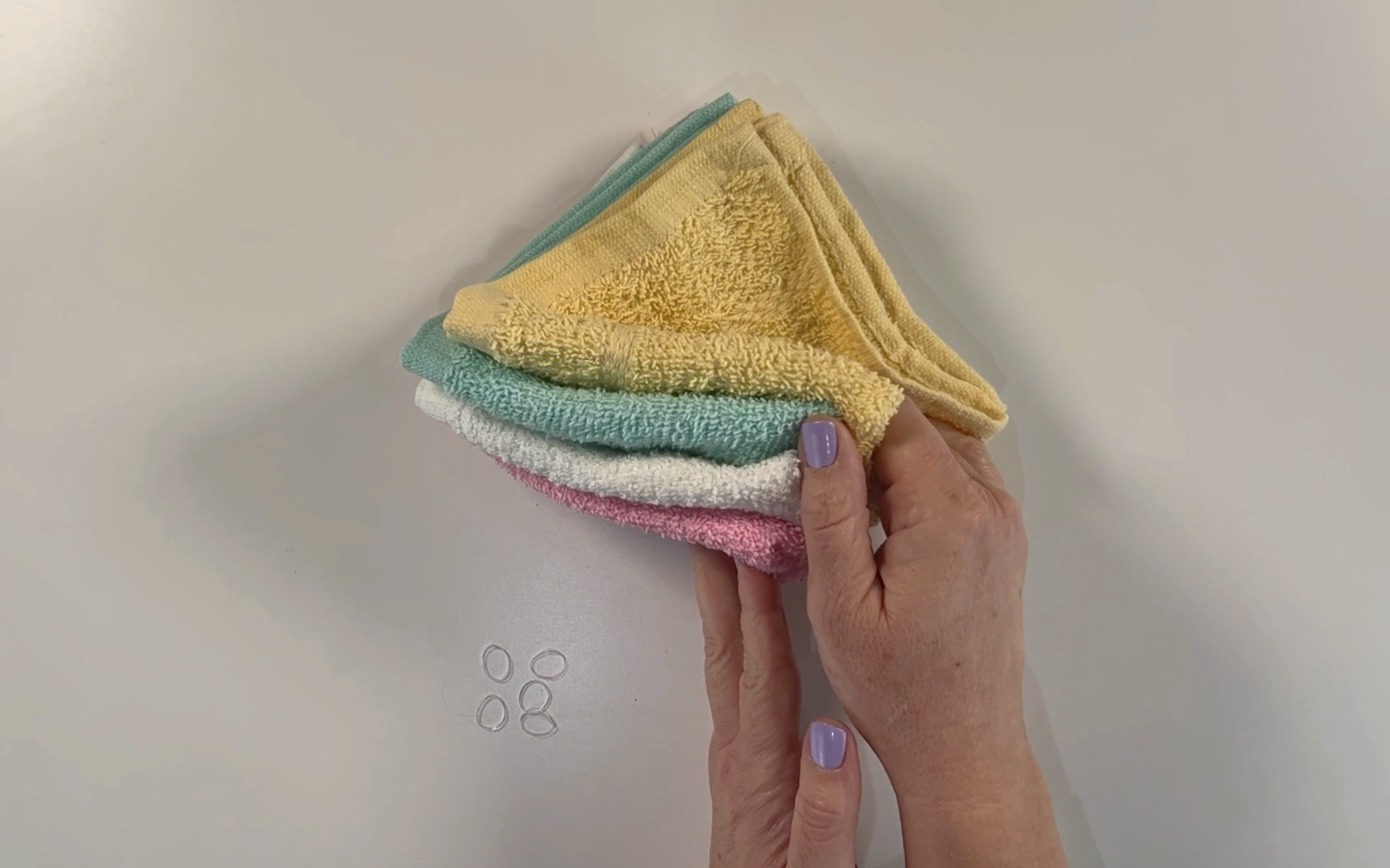 Pink, white, yellow and green washcloths along with clear elastic bands
