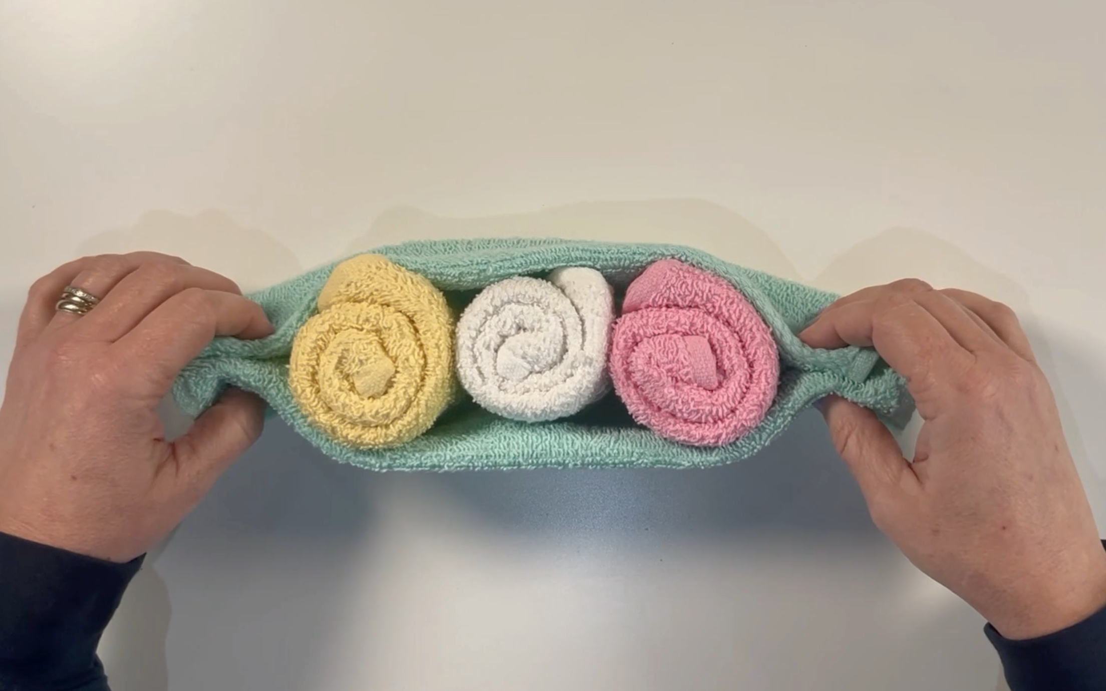 3 rolled washcloths in the middle of the green washcloth. The sides have been folded up to cover the centre washcloths