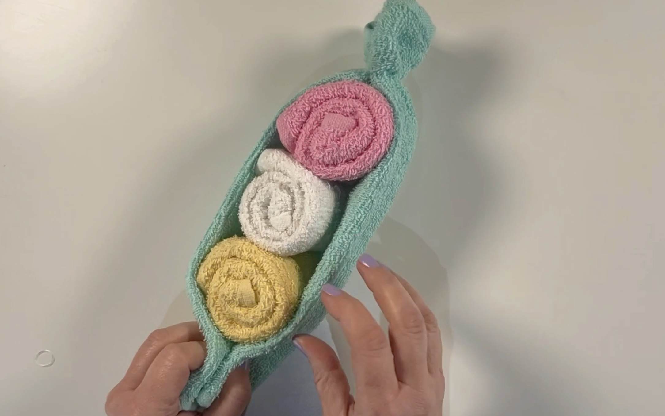 Securing each end of the washcloth with a clear elastic band to make the pea pod.