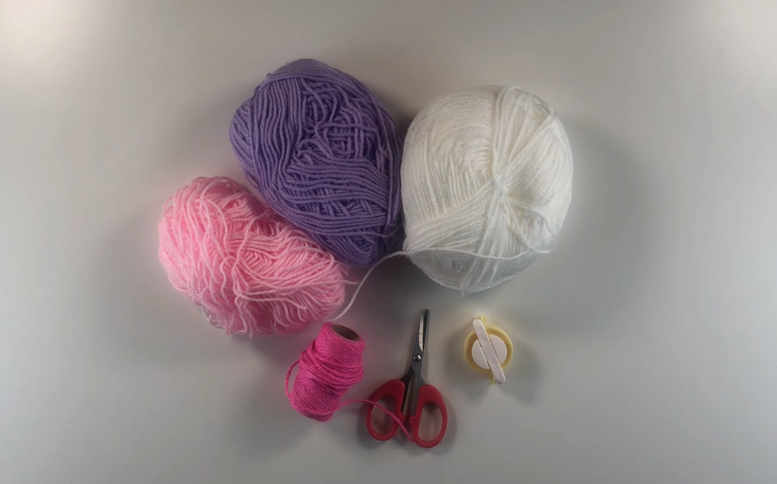 Supplies i used to make pompom gift wrap: white, pink and purple balls of wool.
Scissors, twine and a pompom maker