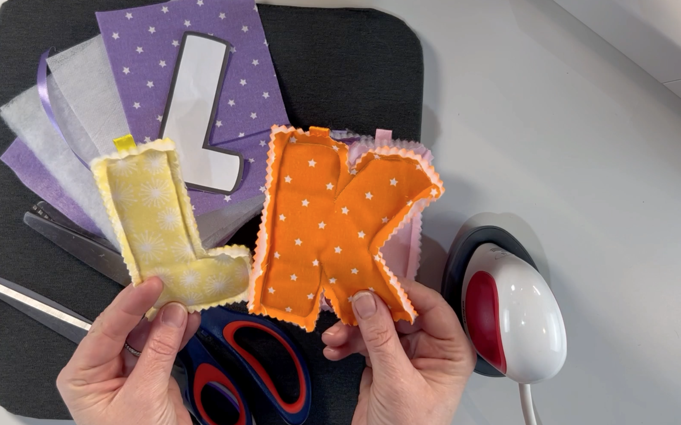 A yellow material padded letter L and an orange material padded letter K that have been sew ready to hang on a banner.