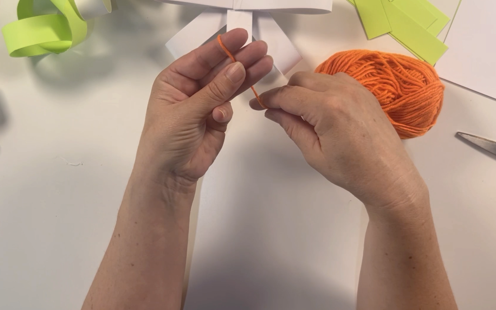Wrapping orange wool around 3 fingers to start to make a pompom