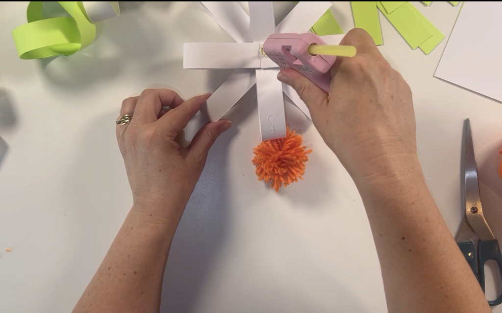Placing hot glue in the centre of the card daisy to attach the pompom
