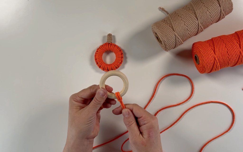 Making a larks head knot through the wooden ring with the orange cord