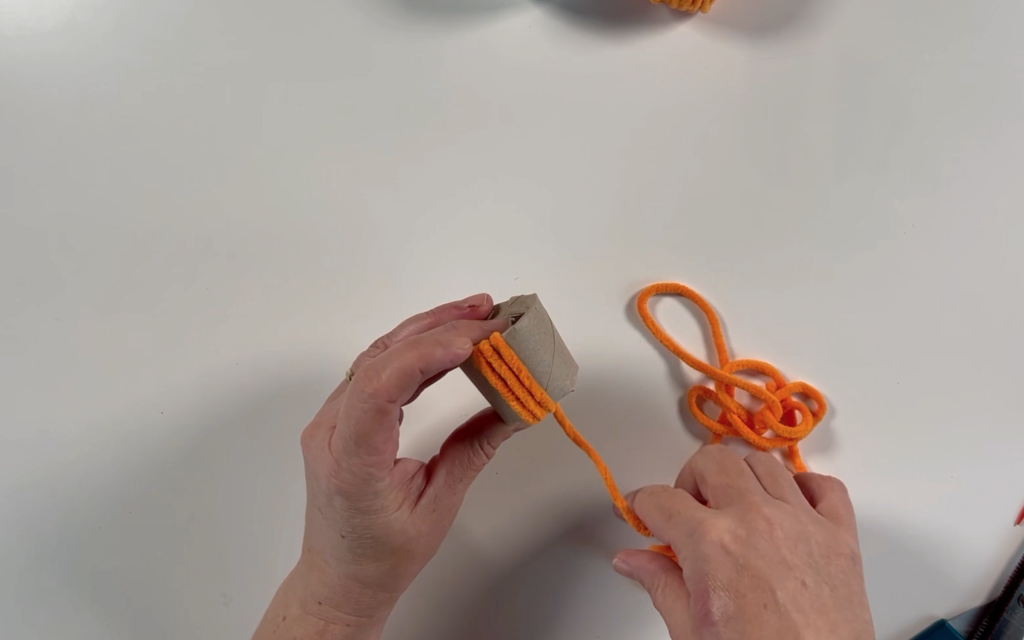 Wrapping orange wool around the toilet roll tube, pushing the wool through the middle of the tube. 
