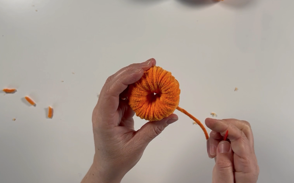 An almost fully wrapped yarn pumpkin. Large eye needle threaded with wool ready to push through the centre of the pompom. 