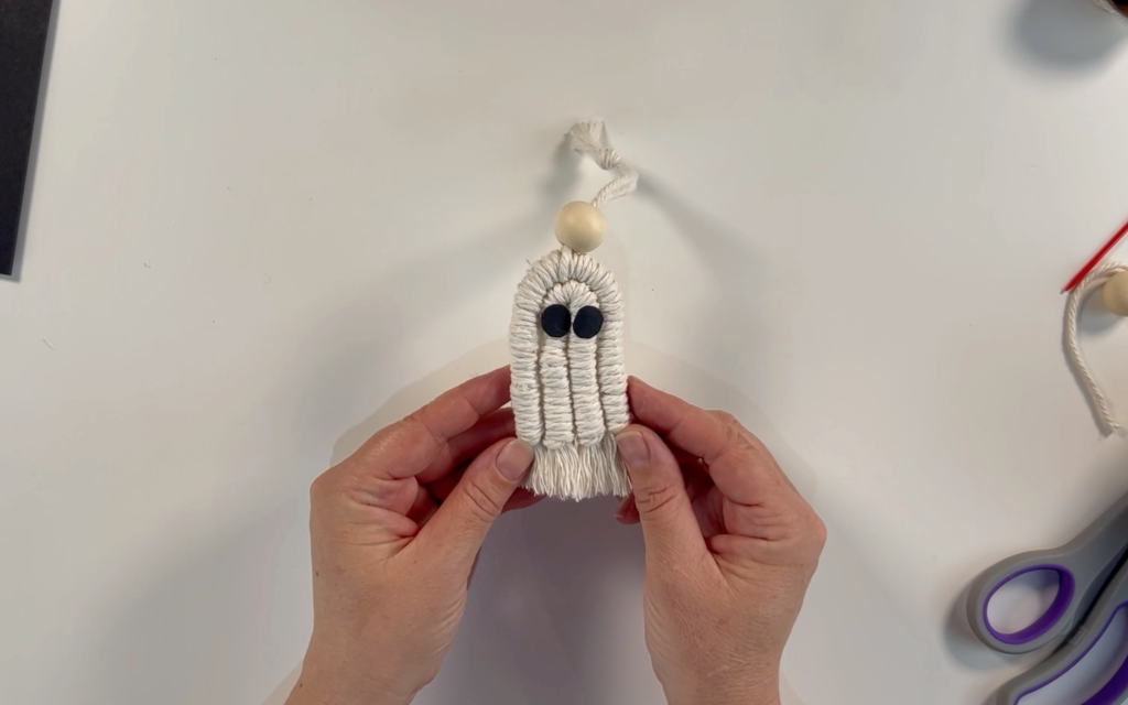 A macrame ghost with a wooden bead at the top and the string tied ready for hanging. 