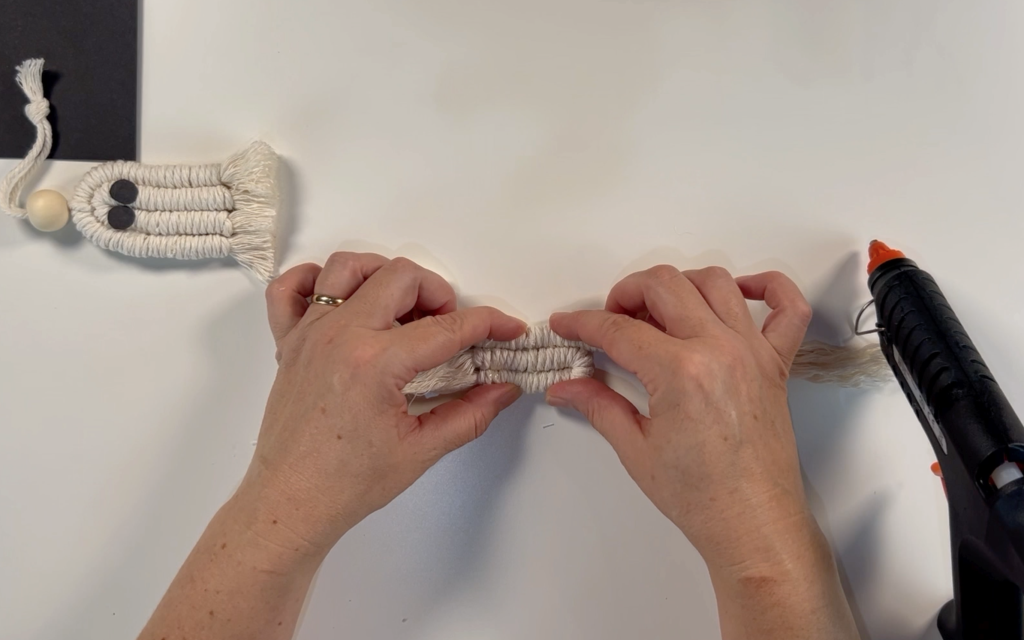 Adding hot glue to the outer side of the folded wrapped cord. Pressing the other strand of wrapped cord onto the folded cord until set
